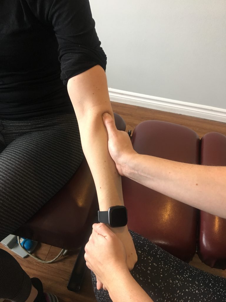 oakville physiotherapist providing active release therapy to a patients elbow by pushing against the muscles of the forearm while holding their hand