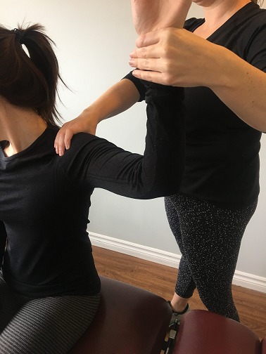 patient sitting while physiotherapist hold arm at an 90 degree angle and treats shoulder