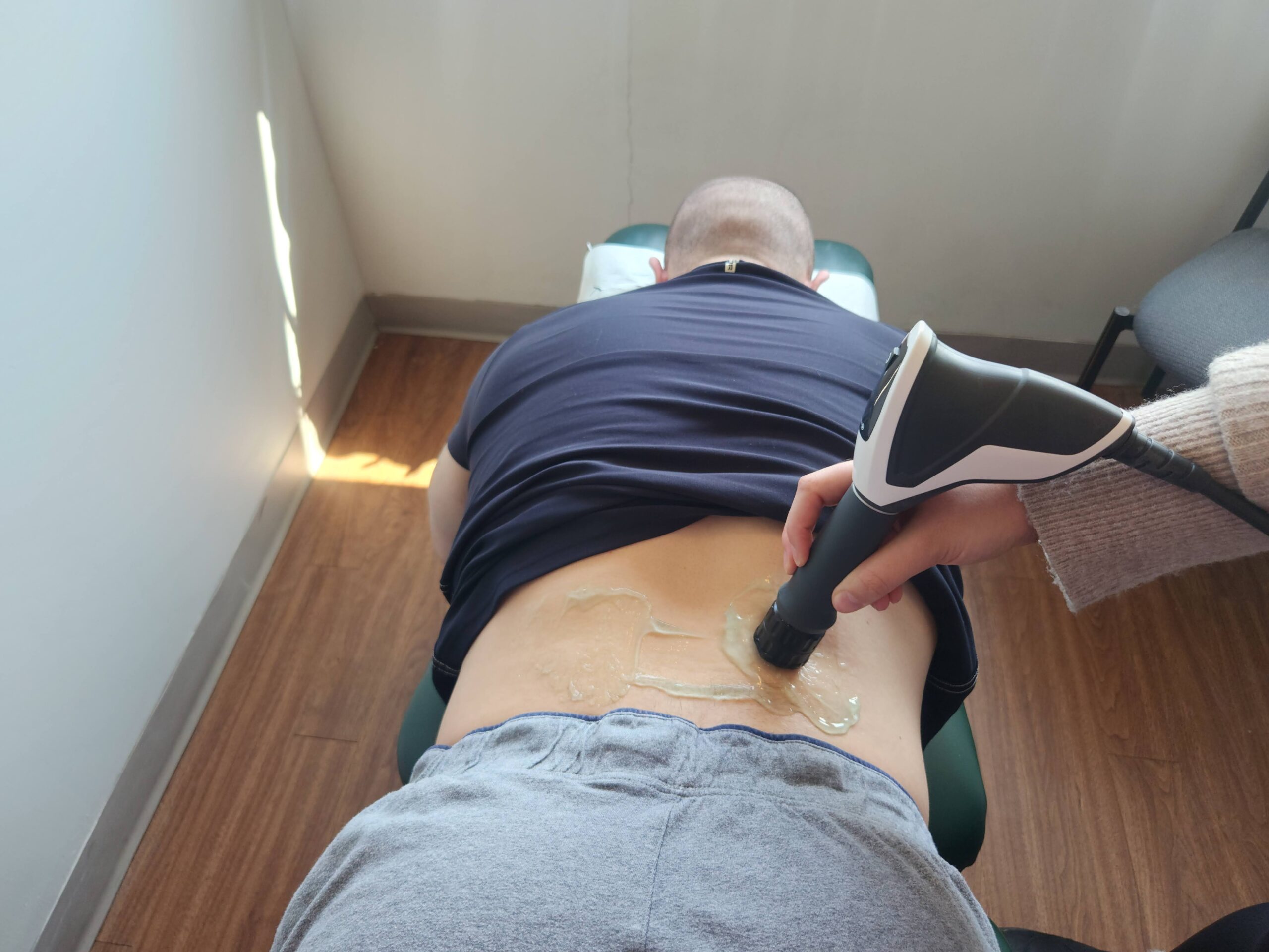 male patient face down getting shockwave therapy on his right low back physiotherapy